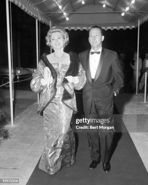 Zsa Zsa Gabor walking under an awning with Wally Sewall in evening attire, Palm Beach, Florida, c1957