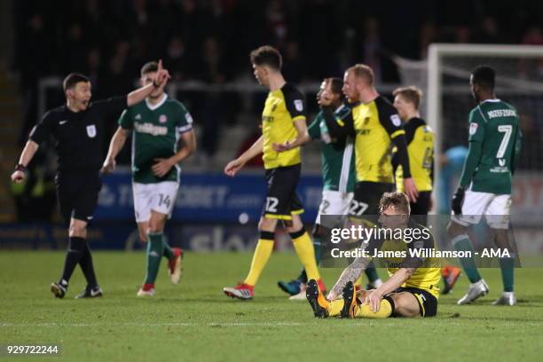 Kyle McFadzean of Burton Albion recovers after being fouled while his teammates hound match referee Tony Harrington to show a second yellow card to...