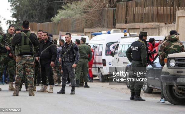 Picture taken on March 9, 2018 shows members of the Syrian government forces waiting next to Syrian Red Crescent ambulances waiting to pass through...