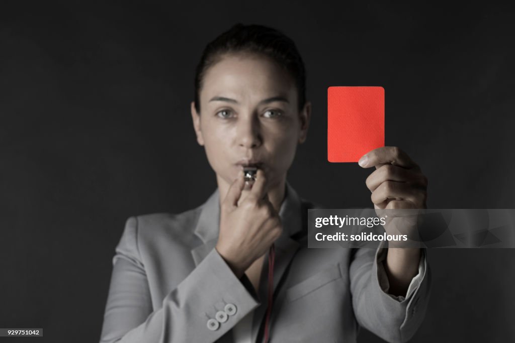Business woman holding red card and blowing a whistle
