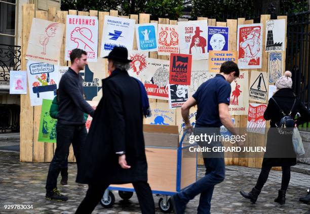 People walk in front of a fence where posters of May 68 are displayed during an exhibition entitled "Mai 68 en 500 affiches" gathered by collector...