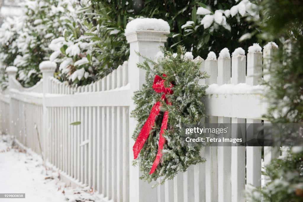 Christmas wreath hanging on white fence covered in snow