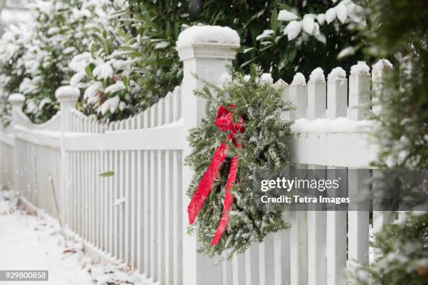 christmas wreath hanging on white fence covered in snow - snowy christmas trees stock pictures, royalty-free photos & images