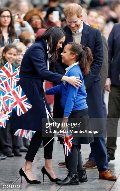 Prince Harry looks on as Meghan Markle hugs a young girl during a walkabout at Millennium Point before attending an event to celebrate International...