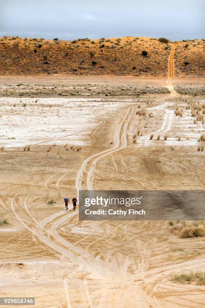 two runners on a red sand track leading through the desert and over a red sand dune. - simpson desert imagens e fotografias de stock