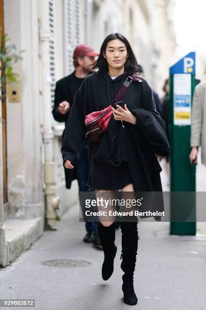 Model wears a red shoulder strap bag, a black hoodie sweater, black thigh high boots, outside APC, during Paris Fashion Week Womenswear Fall/Winter...