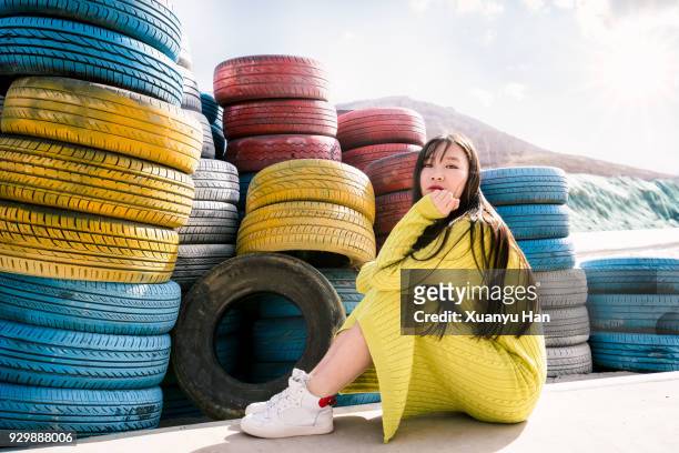 portrait of young woman sitting by the tires - rubber dress stock-fotos und bilder