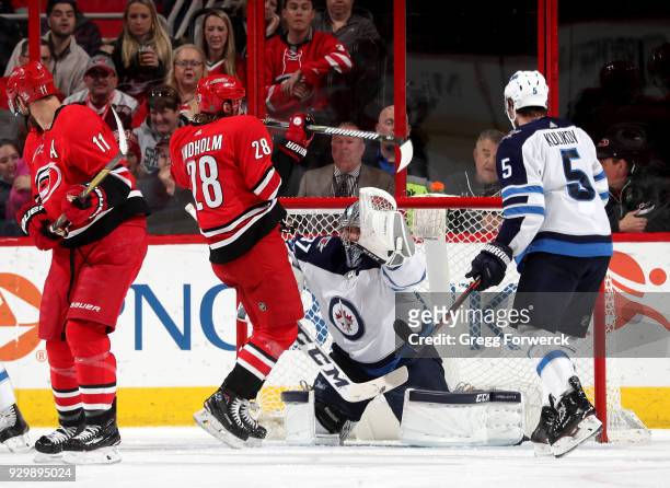 Elias Lindholm of the Carolina Hurricanes creates traffic near the crease in front of Connor Hellebuyck of the Winnipeg Jets who attempts to protect...