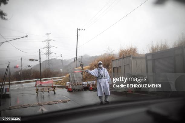 This picture taken on March 5, 2018 shows a guard gesturing at a checkpost exit from the exclusion zone of Futaba town, Fukushima prefecture, as...