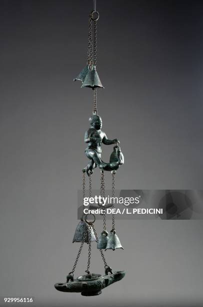 Bronze tintinnabulum, statue of a pygmy holding a large phallus from which a flywheel lamp with three opposing bells and a phallic-shaped amulet are...