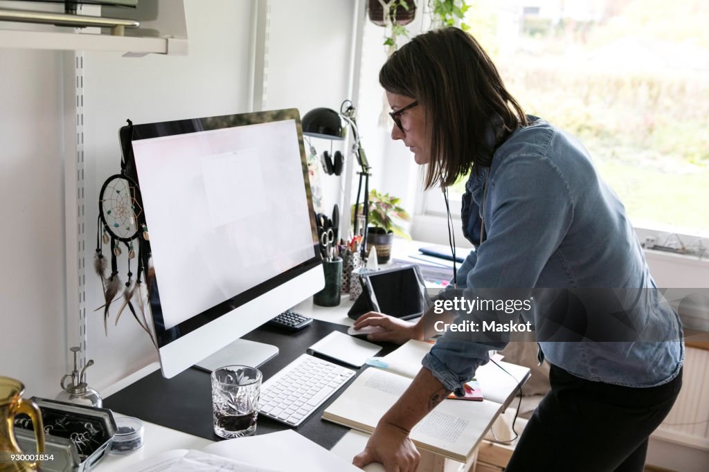 Side view of businesswoman using computer while standing at home