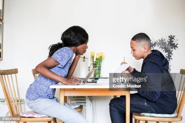 mother helping son doing homework at dining table in house - dining table icon stock pictures, royalty-free photos & images