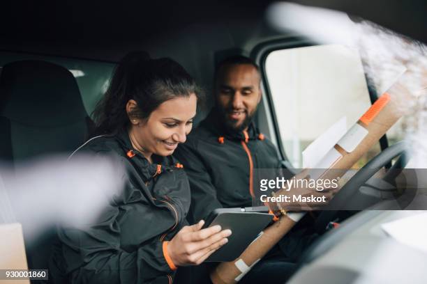 smiling workers looking at digital tablet while sitting in delivery van - repartidor fotografías e imágenes de stock