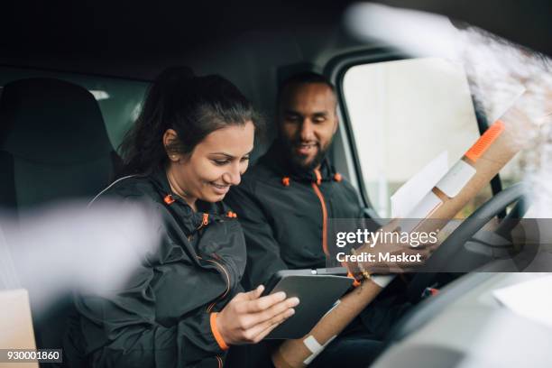 smiling workers looking at digital tablet while sitting in delivery van - delivery driver stockfoto's en -beelden