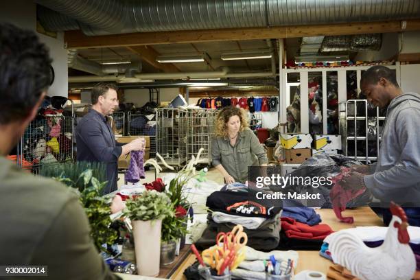 multi-ethnic volunteers examining textiles in warehouse - clothing donation stock pictures, royalty-free photos & images