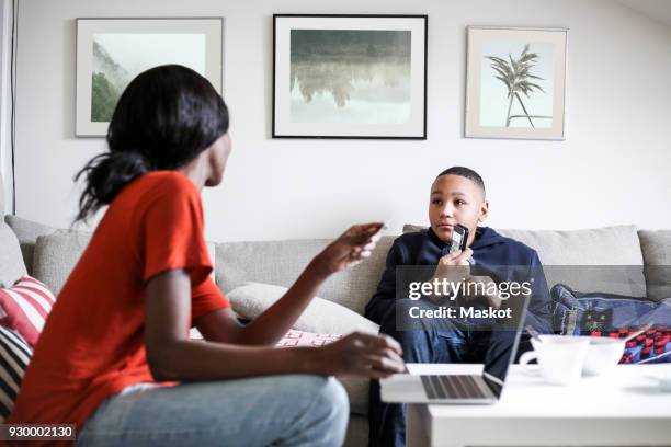 boy showing mobile phone to mother with laptop and credit card in living room - teenager boy shopping stock pictures, royalty-free photos & images