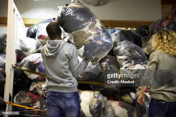 rear view of coworkers stacking plastic sacks in warehouse - clothing donations stock pictures, royalty-free photos & images