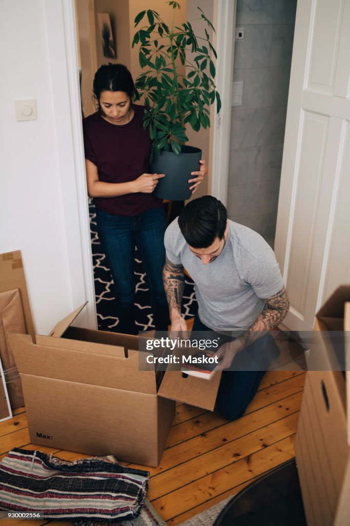 Woman holding potted plant while man reading book during unpacking boxes at house