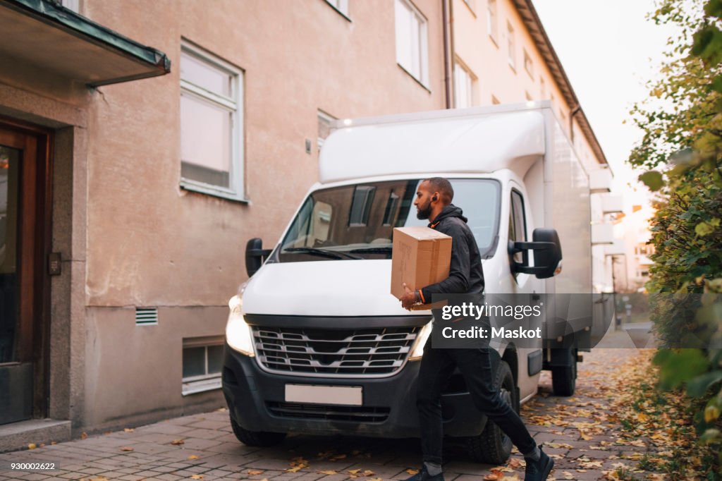 Side view of man carrying box while walking by delivery van in city