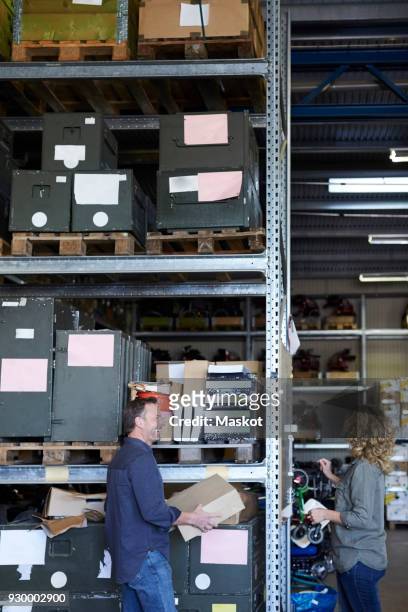 side view of smiling mature male volunteer standing with female colleague by rack at warehouse - tool rack ストックフォトと画像
