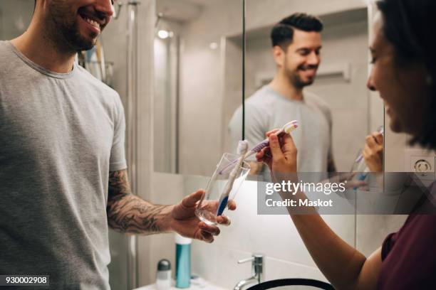 smiling couple arranging toothbrushes in container by mirror in bathroom - change toothbrush stock pictures, royalty-free photos & images