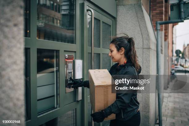female messenger ringing intercom on closed door while carrying box on sidewalk - security doorbell stock pictures, royalty-free photos & images