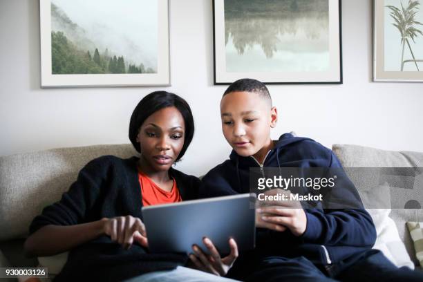mid adult woman with son using digital tablet on sofa at home - parental control stock pictures, royalty-free photos & images