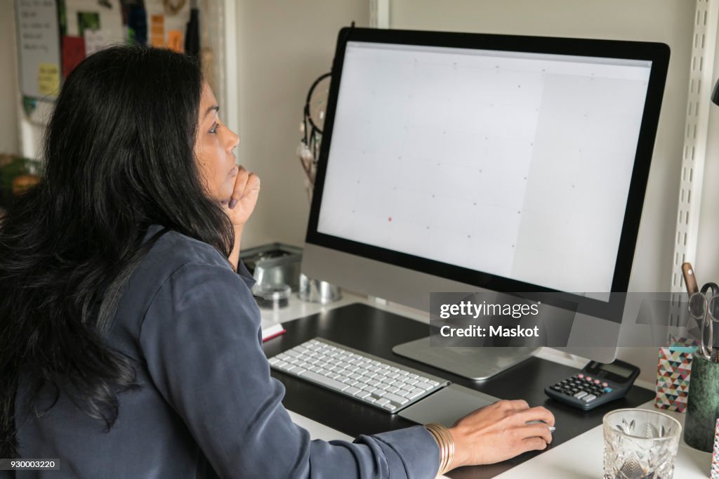 Side view of businesswoman using computer while sitting at home office