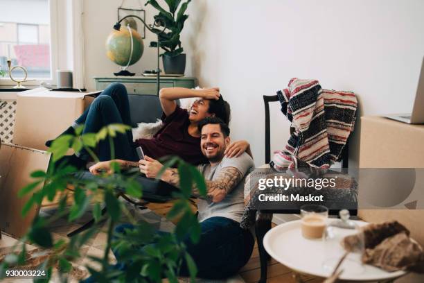 happy couple using smart phone while resting at new home during location - amor proprio photos et images de collection