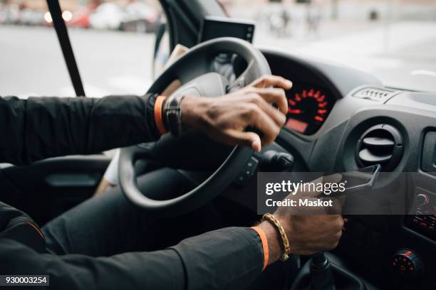 cropped image of man holding mobile phone while driving delivery van - van driver stock pictures, royalty-free photos & images