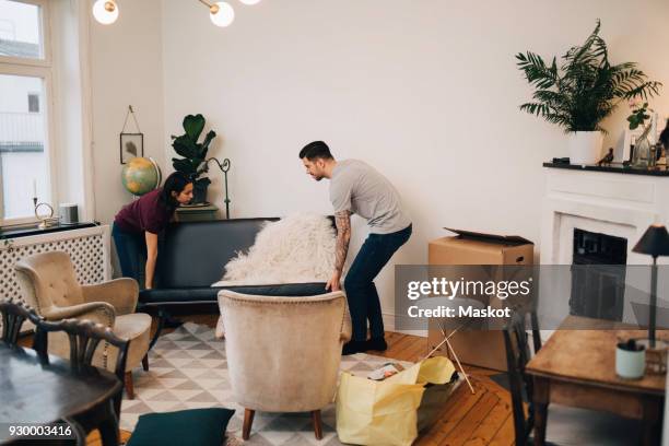 man and woman arranging sofa in living room - movilidad fotografías e imágenes de stock