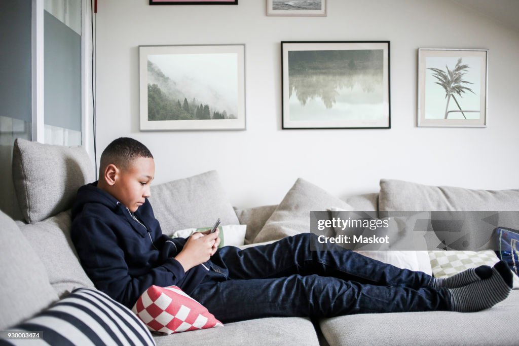 Full length side view of teenage boy using mobile phone on sofa at home