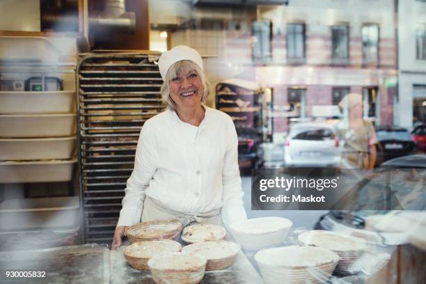 portrait of senior smiling baker at bakery seen from glass window - bakery window stock pictures, royalty-free photos & images