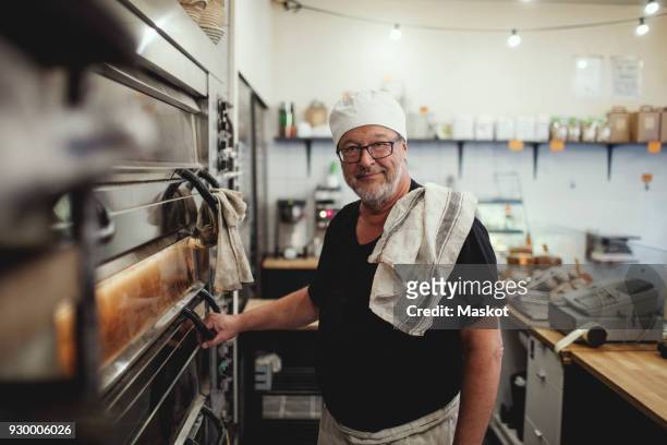 portrait of senior baker standing by oven at bakery - bakery imagens e fotografias de stock