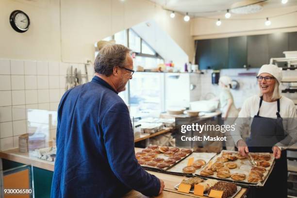 smiling female owner showing fresh baked food to customer at bakery - bakery shop stock pictures, royalty-free photos & images