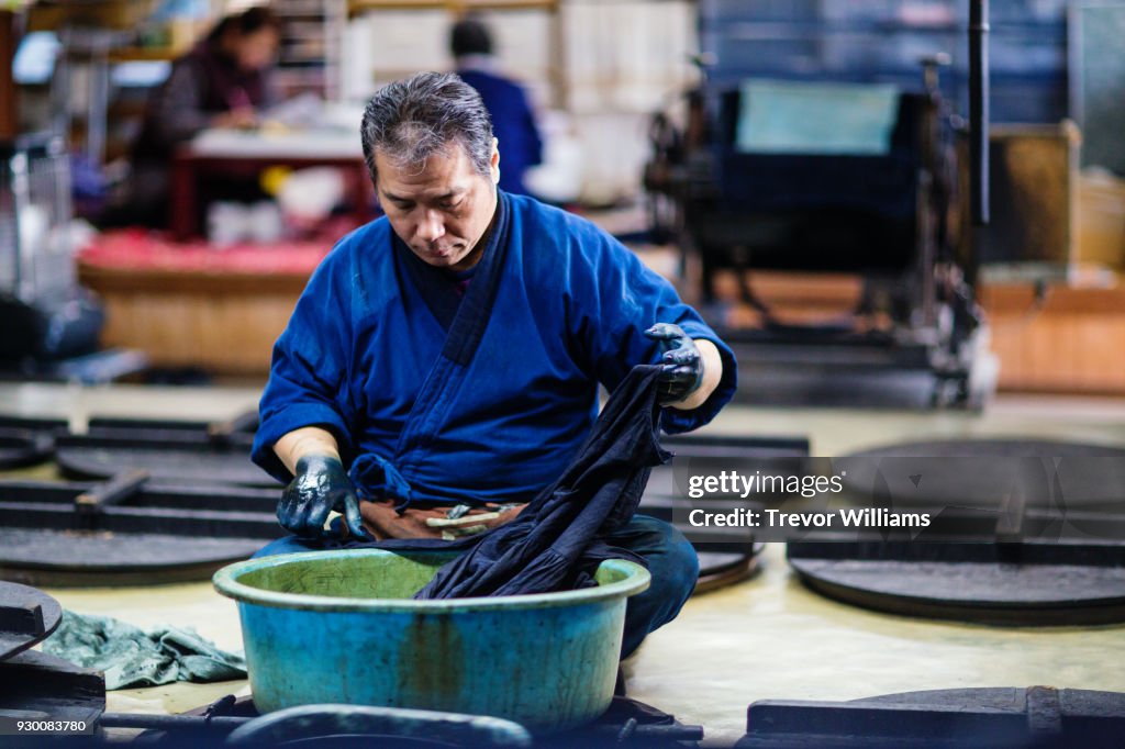 A senior artisan dyeing textiles with traditional indigo dye