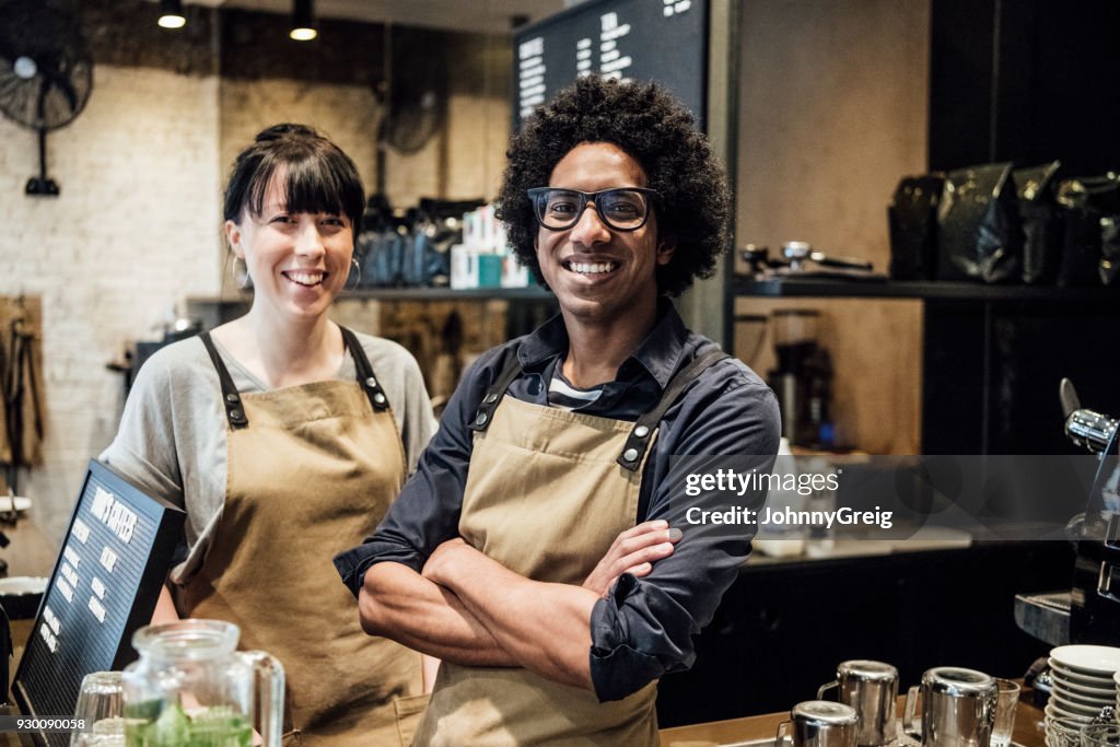 Two colleagues working in coffee shop smiling towards camera