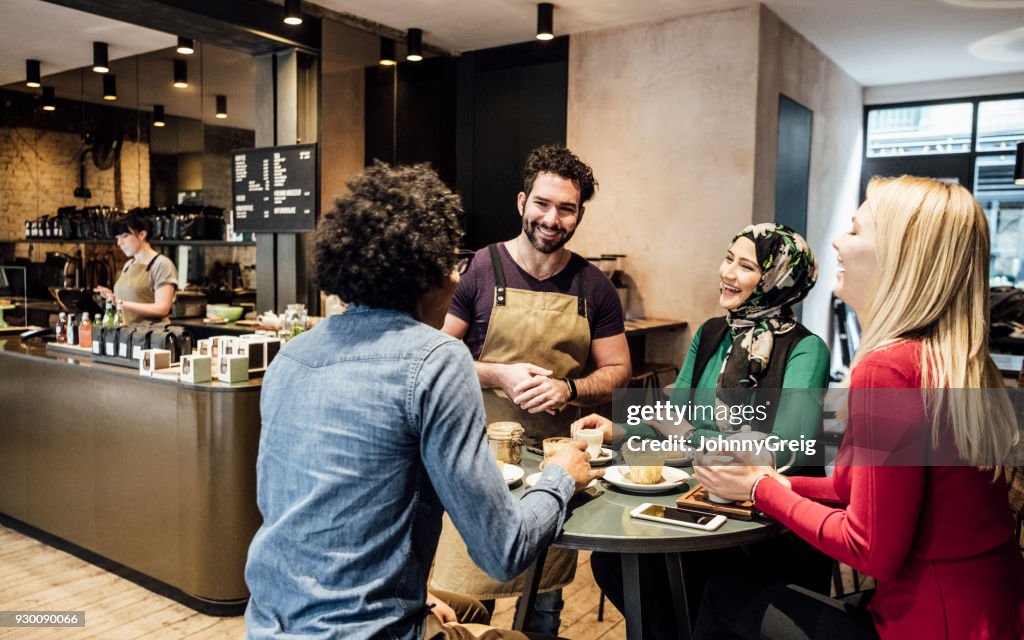 Cheerful waiter talking to thee customers in cafe and smiling