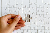 Woman's hand placing put the last white jigsaw puzzle piece to complete the mission, business success concept
