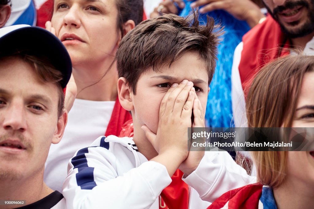 Young football fan covering face during football match