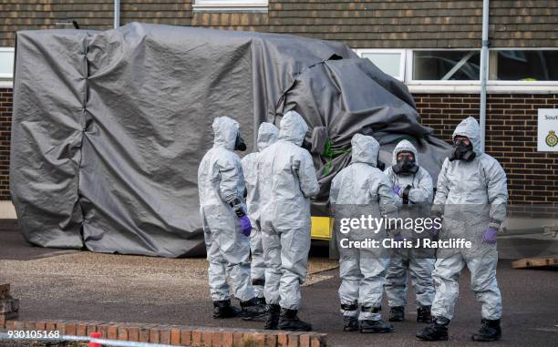Military personnel wearing protective suits cover two ambulances with tarpaulin as they prepare to remove them from Salisbury ambulance station as...