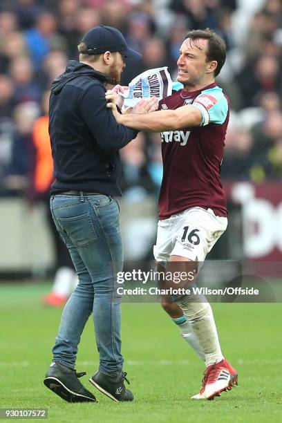 Mark Noble of West Ham fights with a pitch invader protesting the board of directors during the Premier League match between West Ham United and...