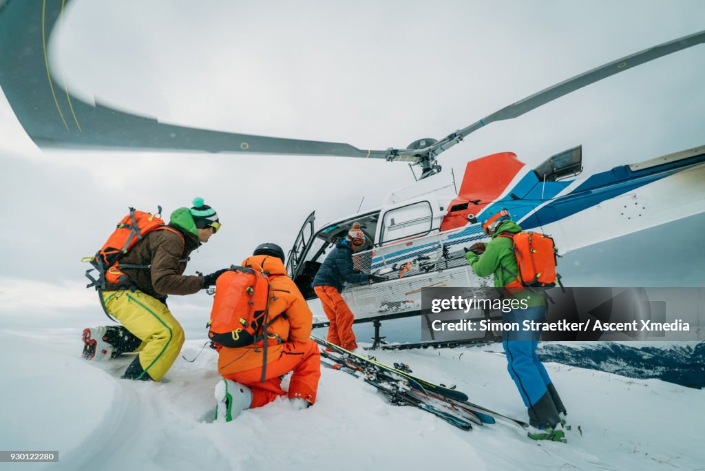 Heli-skiers disembark from helicopter, on snow crest