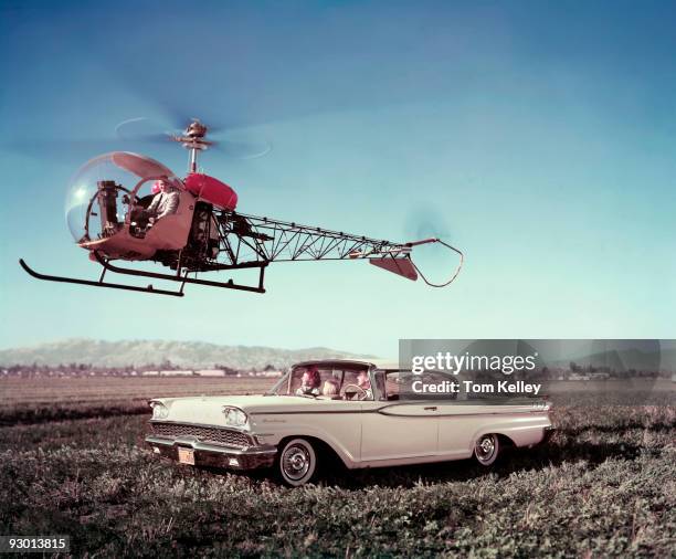 Family riding in a Ford Monterey automobile watches a helicopter fly above them in an open field in California, 1959.