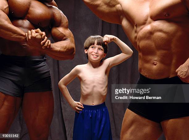 young boy making muscles with body builders. - slim stock pictures, royalty-free photos & images