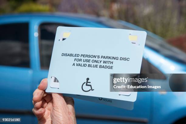 Woman's hands holding a Blue Badge parking disc issued in the UK to disabled drivers.