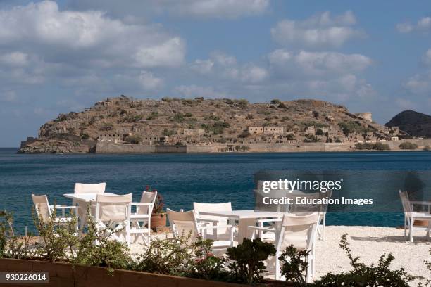 Tables and chairs overlook Spinalonga Island from Plaka a northern Crete seaside resort.