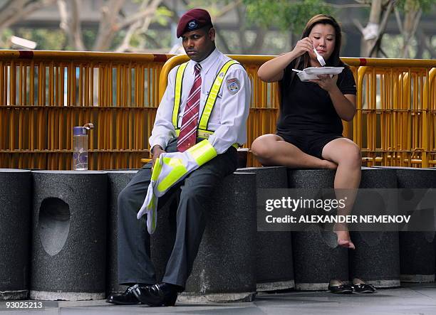 Singaporean security officer looks on as a woman enjoys a snack in front of The Suntec Centre, the venue for the Asia-Pacific Economic Cooperation...