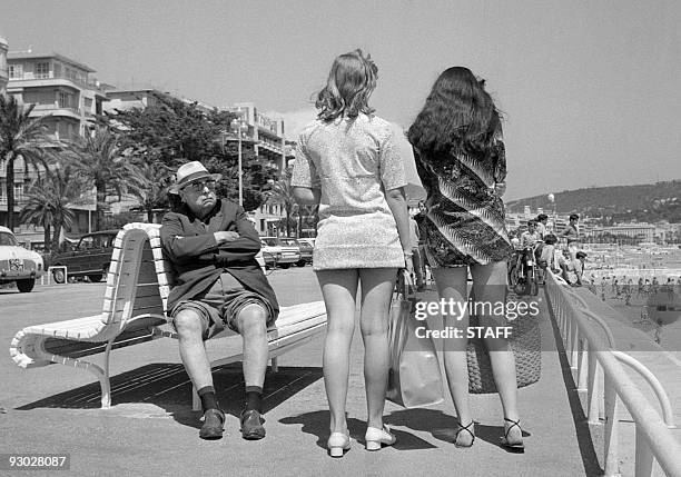 His trousers' legs rolled to take advantage of the sun, a retired man looks toward two girls wearing mini-skirt, 13 July 1969 in Nice.