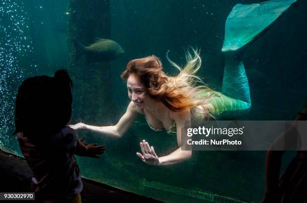 Visitors watch mermaid, as she swims with fish in a giant tank during a show at an aquarium in Sao Paulo, Brazil, on March 11, 2018.